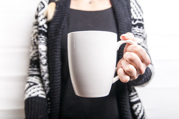 Female hand holding white cup in black patterned sweater background. Copy space