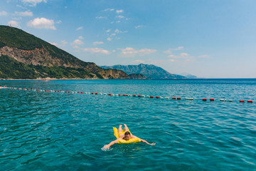 young adult man swimming on yellow inflatable mattress in blue sea.