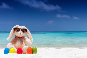 Osterhase mit Sonnenbrille und bunten Ostereiern relaxt im Urlaub am tropischen Strand