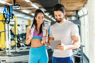 Bearded smiling personal trainer showing woman results of training on tablet. Woman standing next...
