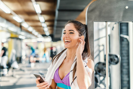 Close up of smiling Caucasian woman choosing music on smart phone while standing in a gym. Towel around neck.