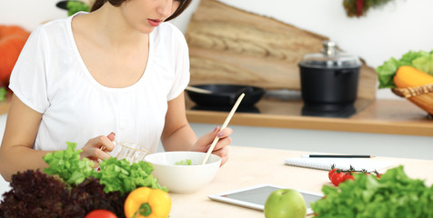 Beautiful Hispanic woman cooking in kitchen while using tablet computer and wooden spoon. Housewife found new recipe for dinner or breakfast. Healthy meal and householding concepts