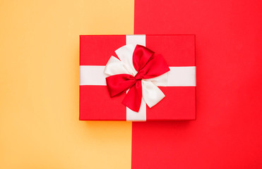 Real box with white and red bow and ribbon top view on Valentine's day isolated on half red and yellow background. Flat lay. Copy space.