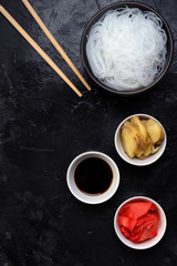 Chinese glass noodles with ingredients for cooking, vegetables and spices, ginger and soy sauce on black background top view