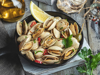 Cooked seafood clams in the iron pan portion with lemon and seasoning - Powered by Adobe