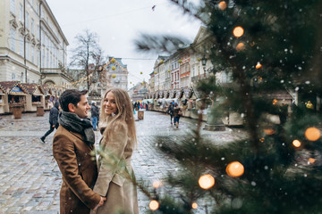 Obraz na płótnie Canvas Beautiful romantic lovely couple laughing and have fun on the central square of the Christmas Europe city