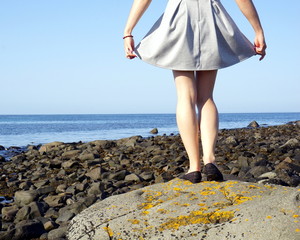 Young girl stands on big stone by the ocean