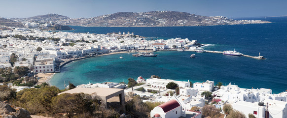 panoramic view of the Mykonos town harbor with famous windmills from the above hills on a sunny...