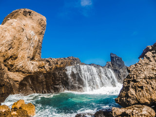 When the sea gets rough the waves are breaching the rocks splashing over their surface and creating a temporary waterfall. This phenomena is on the island of Lombok(next to Bali) in Indonesia.