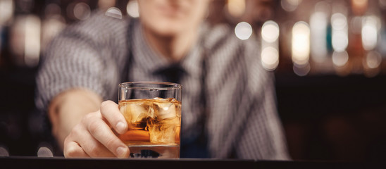 Barman holds out glass of whiskey with ice to male visitor. Concept rest in bar