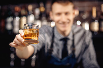 Barman holds out glass of whiskey with ice to male visitor. Concept rest in bar