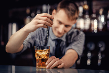 Barman prepares alcoholic cocktail in bar and with ice. Dark background
