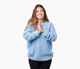 Young beautiful brunette woman wearing blue winter sweater over isolated background begging and praying with hands together with hope expression on face very emotional and worried