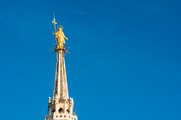 Fototapeta na wymiar Golden statue of Virgin Mary called Madonnina, placed on the roof of Duomo cathedral, is the symbol of Milan, Italy