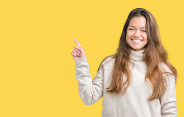 Young beautiful brunette woman wearing turtleneck sweater over isolated background with a big smile on face, pointing with hand and finger to the side looking at the camera.