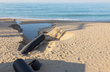 Fototapeta na wymiar Industrial wastewater, the pipeline discharges liquid industrial waste into the sea on a city beach. Dirty sewage flows from a plastic sewer pipe onto the sand of a sea city beach