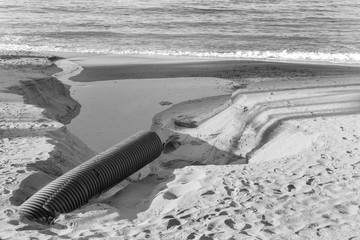 Industrial wastewater, the pipeline discharges liquid industrial waste into the sea on a city beach. Dirty sewage flows from a plastic sewer pipe onto the sand of a sea city beach