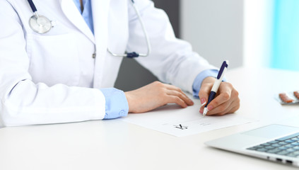 Female doctor filling up prescription form while sitting at the desk in hospital closeup.  Healthcare, insurance and excellent service in medicine concept 