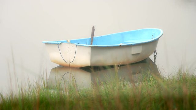 Dinghy rowboat at anchor in a quiet foggy cove with no horizon line visible. Great background for graphics or title page. Wetland grass in foreground.