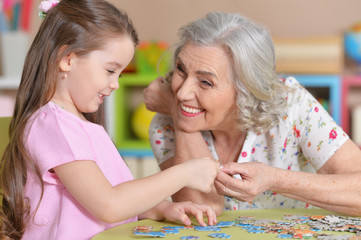 Fototapeta premium Cute little granddaughter and grandmother collecting puzzles