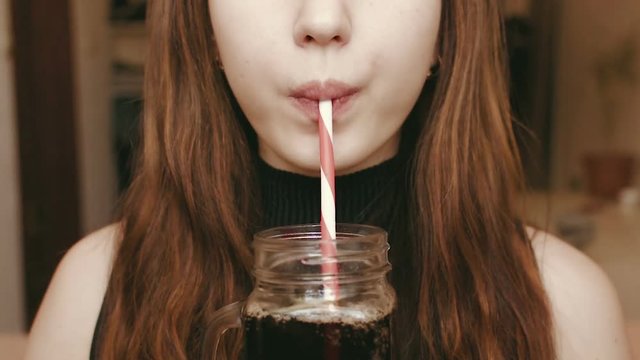 A young girl drinks a fizzy drink through a straw. Face close up. HD