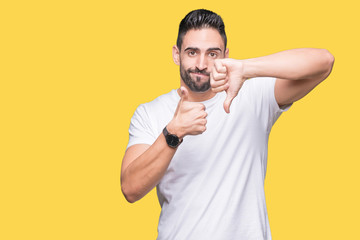 Handsome man wearing white t-shirt over yellow isolated background Doing thumbs up and down, disagreement and agreement expression. Crazy conflict
