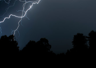 lightsning striking over trees during a night storm