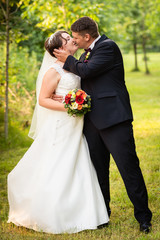Gl&uuml;ckliches Brautpaar beim spazieren und k&uuml;ssen am Hochzeitstag im Park, Wald