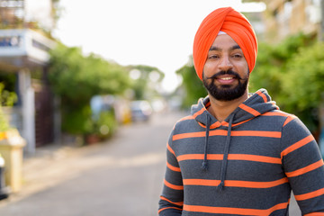 Happy Indian Sikh man smiling outdoors and wearing orange turban