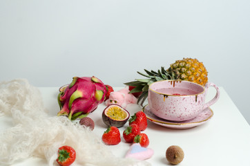 A letter paper for Valentine's day with a hearts, cup of fruit tea, passion fruit, strawberries, pitahaya, lychee on white table. Top View.