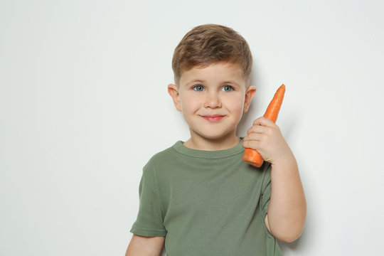 Adorable little boy with carrot on white background. Space for text