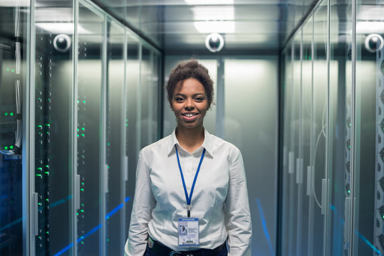 Adult IT worker in white shirt standing among server racks in data center smiling at camera