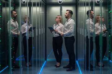 Wide shot of workers with digital tablet in hand in a data center walking between rows of server racks