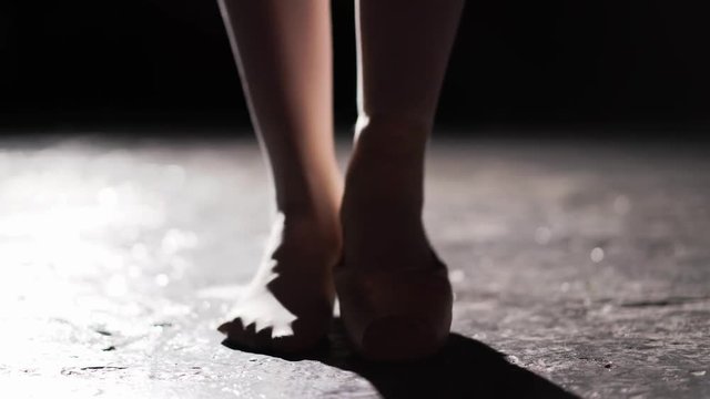 Close up of female legs standing in pose in spotlight on black background in studio. One feet in pointe and another feet without shoe on the toes.