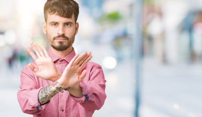 Young handsome man wearing pink shirt over isolated background Rejection expression crossing arms and palms doing negative sign, angry face