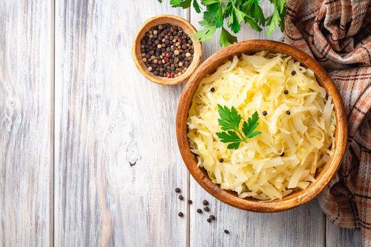 Homemade sauerkraut with black pepper and parsley in wooden bowl on rustic background. Top view. Copy space.