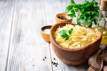 Homemade sauerkraut with black pepper and parsley in wooden bowl on rustic background. Selective...