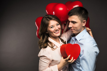 Fototapeta na wymiar Young couple with heart shaped red balloons near grey wall