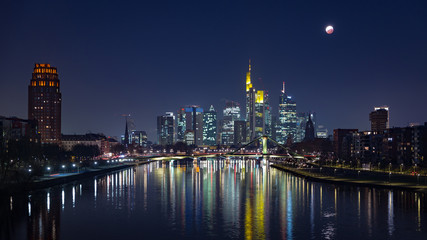 Fototapeta na wymiar End of lunar eclipse of over the skyline of Frankfurt, Germany, with reflections on the river Main.