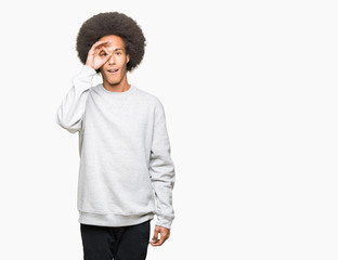 Fototapeta na wymiar Young african american man with afro hair wearing sporty sweatshirt doing ok gesture shocked with surprised face, eye looking through fingers. Unbelieving expression.