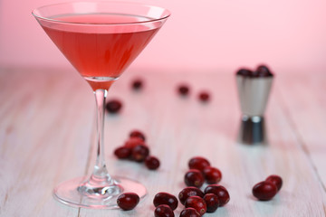 Cosmopolitan cocktail with cranberries, shaker and jigger. White wooden background, pink light, high resolution