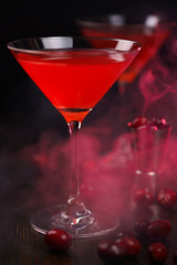 Cosmopolitan cocktail with cranberries and jigger on a dark wooden table. High resolution, red smoke
