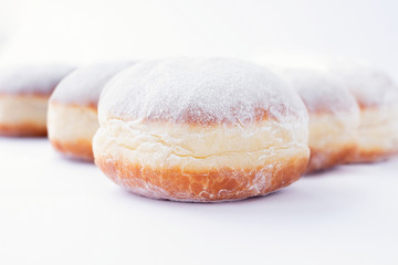 Freshly made doughnuts filled with jam and covered in powdered sugar on a white background