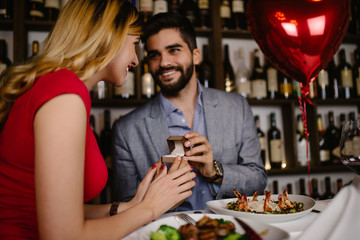 Handsome man proposing a beautiful woman to marry him in restaurant during date.