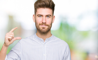 Young handsome man smiling and confident gesturing with hand doing size sign with fingers while looking and the camera. Measure concept.