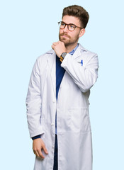 Young handsome scientist man wearing glasses with hand on chin thinking about question, pensive expression. Smiling with thoughtful face. Doubt concept.