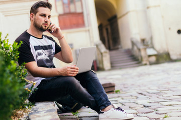Obraz premium Young freelancer with laptop and smartphone working in old city center
