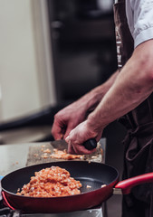 Red Pan with Pile of Cut Salmon Pieces in the Foreground, Male Chef Cutting Fresh Salmon on the Wooden Board in the Background - Isolated Action with Only Hands Showing, Kitchen Set