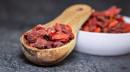 Goji berries in bowl and wooden spoon on dark background - medicine alternative