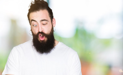 Young hipster man with long hair and beard wearing casual white t-shirt making fish face with lips, crazy and comical gesture. Funny expression.